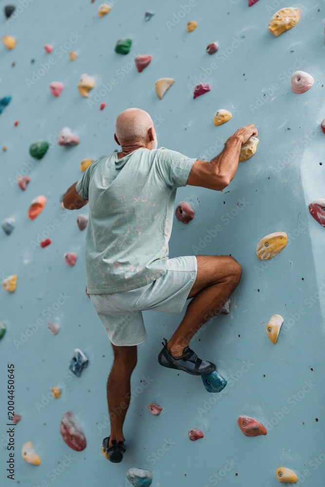 Fototapeta premium Bald man ascending indoor climbing wall during training session