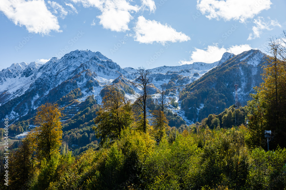 Obraz premium Mountains stand tall under blue sky with clouds in the distance and trees in the foreground