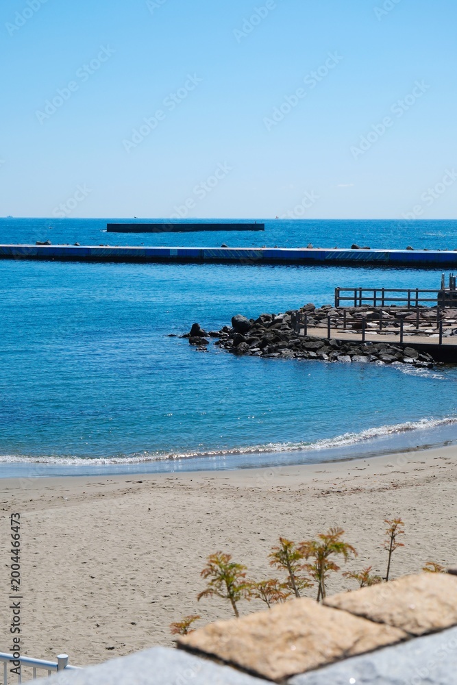 Fototapeta premium Serene sandy beach with blue ocean and distant pier on a sunny day.