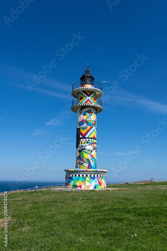 Ajo lighthouse stands on a green cliff, showcasing vibrant abstract art against a blue sky faro de ajo punta del caballo