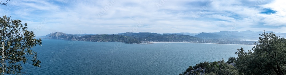Fototapeta premium Panoramic view showing the bay, coastline, town, and mountains under a blue sky laredo cantabria spain