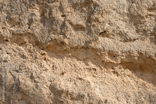 Textura de pared de tierra seca y erosionada con relieves arenosos bajo luz solar directa.