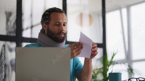 Man in cervical neck collar reading hospital bill letter, shocked by high costs
