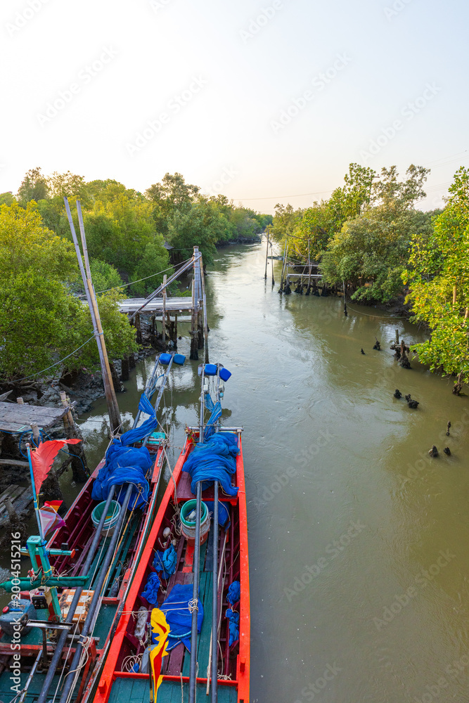 Fototapeta premium Traditional Thai long-tail fishing boats moored in a mangrove forest canal at sunset,High-angle view of two colorful wooden fishing boats docked along a narrow tidal canal surrounded by lush mangrove