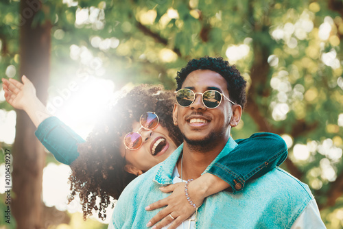 Vászonkép Young couple smiling and having fun outdoors in a sunny park, wearing sunglasses
