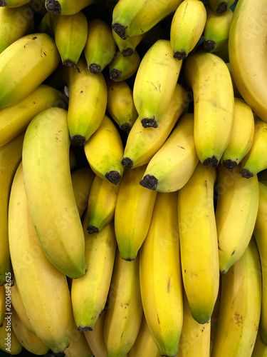 Obraz na plátně Close‑up view of a dense bunch of ripe yellow bananas with slight green tips, arranged tightly together, creating a bright, natural food texture and pattern