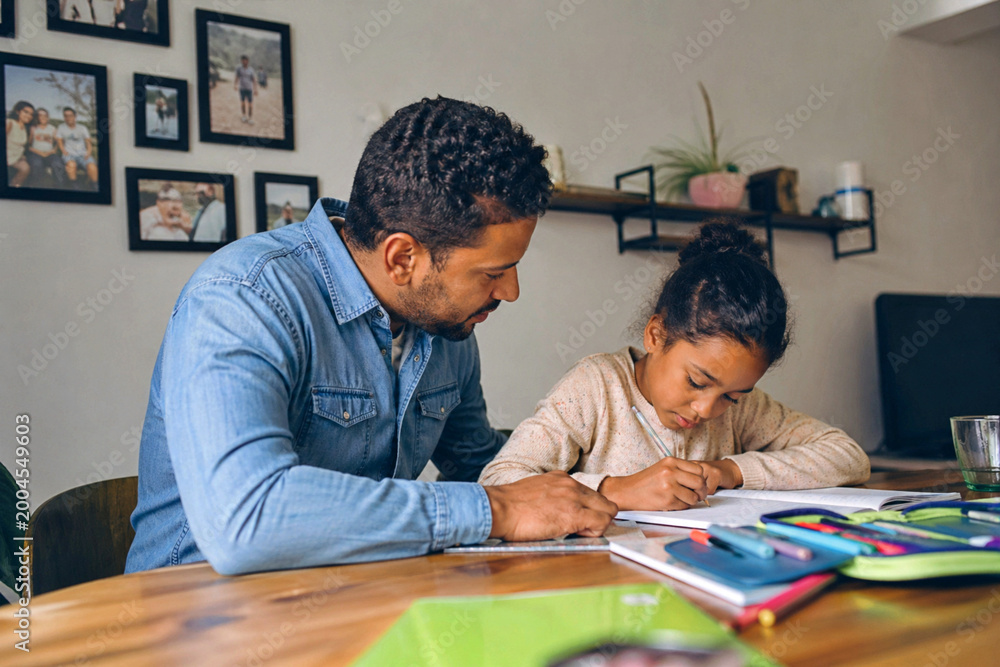 Naklejka premium Vater unterstützt seine Tochter bei den Hausaufgaben am Tisch, konzentriertes Lernen in gemütlicher Wohnatmosphäre, Bildung und Familienzeit im Alltag.