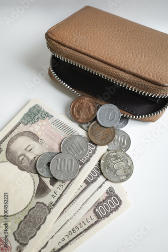 Close-up of a brown leather wallet with Japanese yen banknote and coins scattered on a clean white background, lifestyle manage money concept 
