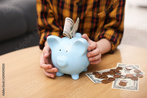 Schilderij op canvas Little boy with piggy bank and money at wooden table indoors, closeup