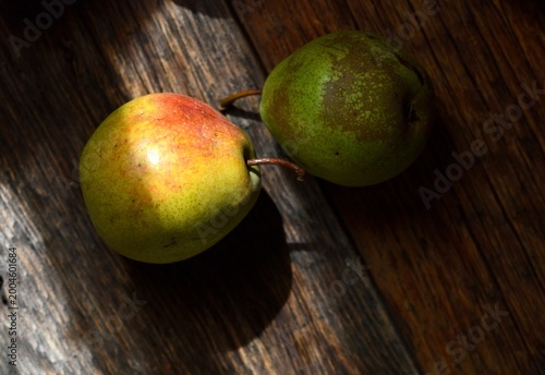 Fresh green and red pears on a rustic dark wooden table in natural morning light.
