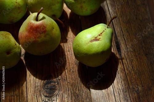 Fresh green and red pears on a rustic dark wooden table in natural morning light.