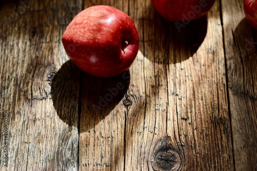 Top view of ripe red apples on a rustic wooden table with dramatic natural lighting and shadows.