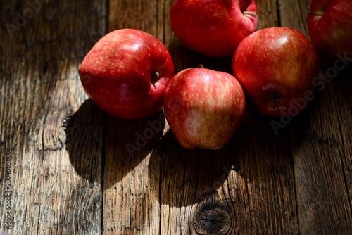 Top view of ripe red apples on a rustic wooden table with dramatic natural lighting and shadows.