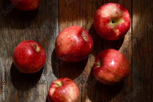 Top view of ripe red apples on a rustic wooden table with dramatic natural lighting and shadows.
