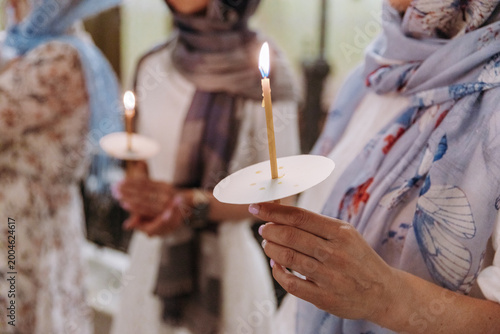 Bild auf Leinwand Women with covered heads holding lit wax candles during a religious ceremony inside an Orthodox church