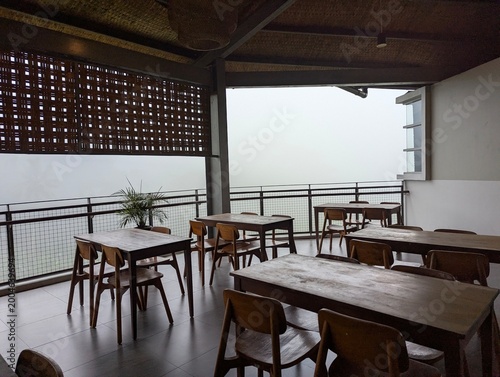 Cozy semi-outdoor cafe interior with wooden tables and chairs, featuring a minimalist industrial design and a scenic foggy balcony view, perfect for relaxing atmosphere and coffee shop background.