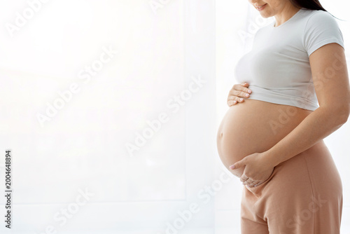Fotografie Closeup side profile of pregnant woman holding bare round belly with both hands