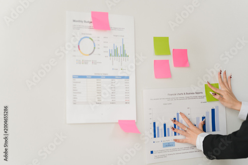 Tableau sur toile Business Chart Examination: An individual meticulously examines financial charts affixed to a wall, accompanied by colorful sticky notes, symbolizing focused analysis and strategic planning