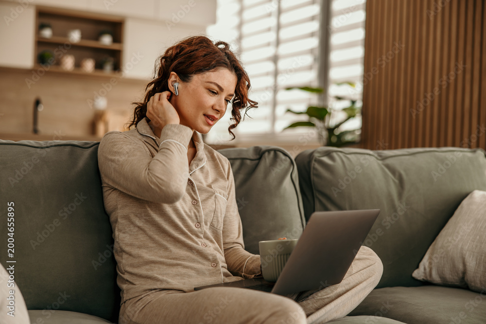 Fototapeta premium Woman working remotely at home wearing pajamas with laptop