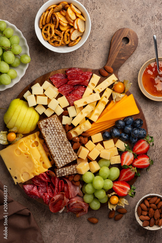 Cheeseboard with berries, nuts, salami, ham, grapes, physalis and honeycomb on a brown background.  Top view. A festive party appetizer