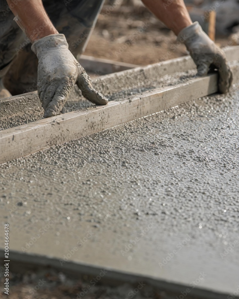 Fototapeta premium Construction worker using a wooden screed to level fresh wet concrete.