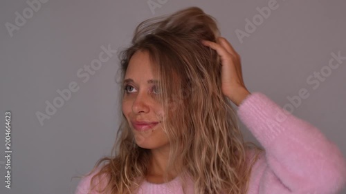 Young blonde woman lifting wavy hair styled with curly method, showing natural volume and texture. Soft pink cozy sweater, healthy haircare routine and modern beauty concept
