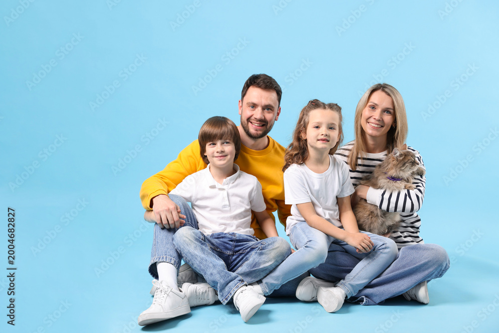 Fototapeta premium Happy family with their cute cat on light blue background, space for text. Adorable pet