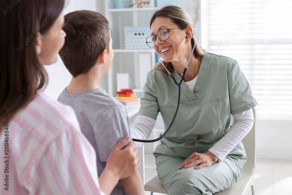 Fototapeta premium Mother with her little son having appointment with doctor in hospital. Nurse checking child with stethoscope