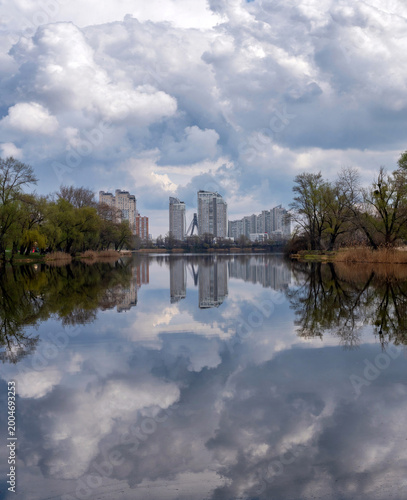 Kyiv 2026: Urban Skyline Reflected in Calm Lake Waters on Cloudy Spring Day