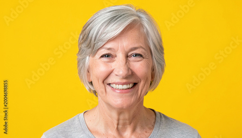 A cheerful older woman with grey hair and a joyful expression. She is wearing a beige shirt.