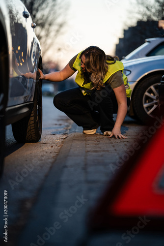 Billede på lærred Woman checking car tire after breakdown on roadside
