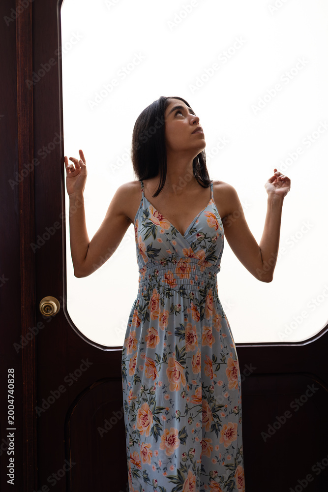 Obraz premium Elegant woman posing by a historic wooden entrance with bright natural lighting and refined architectural details.
