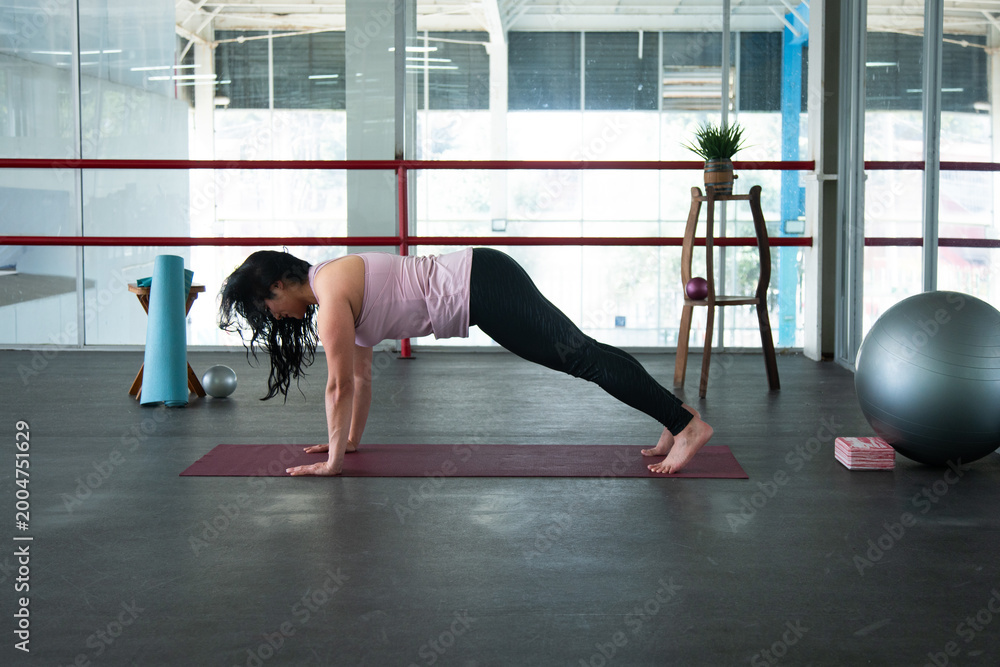 Obraz premium Woman exercising plank pose on yoga mat indoors