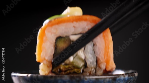Dip one sushi roll in soy sauce on dark background. Closeup

