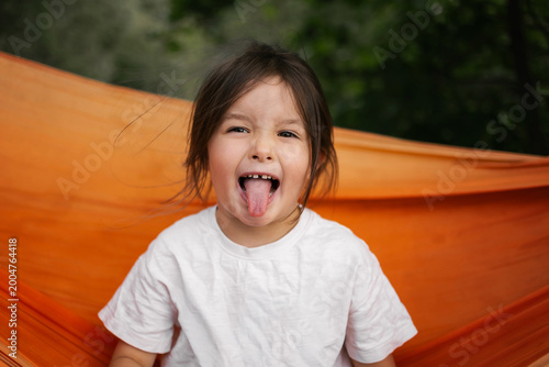 Young girl laughs happily in orange hammock outdoors surrounded by green trees