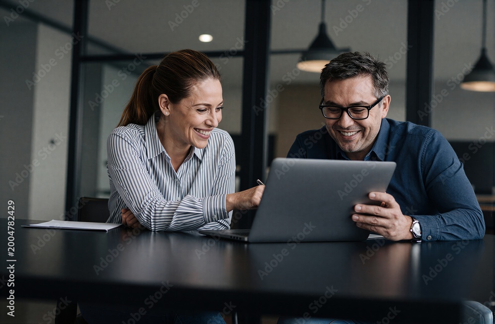 Fototapeta premium Two professionals collaborate happily over a laptop in a modern