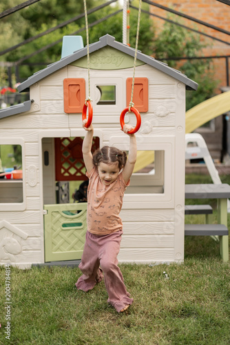 14.05.25 Kyiv, Ukraine: Young child playing on outdoor swing set near colorful plastic playhouse in grassy yard