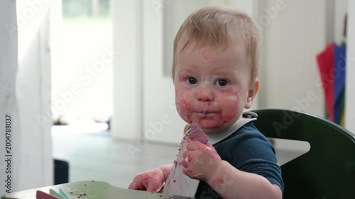 Messy Infant indulges in sweet treat during mealtime. Curious baby eating cookie at home in high chair