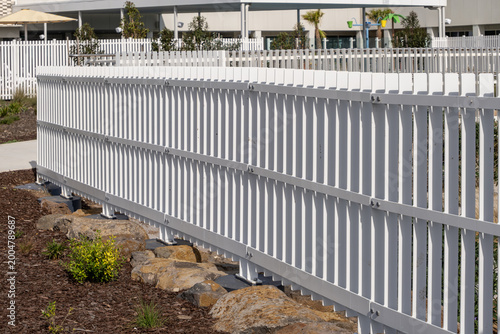 Foto A long white metal palisade fence runs diagonally through the frame alongside a landscaped garden bed