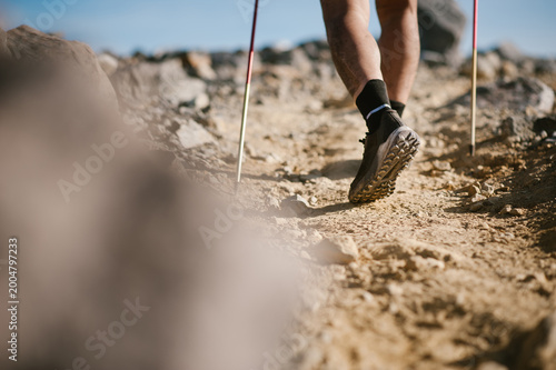 Trail runner legs, shoes and poles on a rocky mountain path