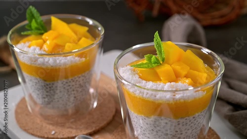 Creamy chia seed pudding layered with bright mango puree and fresh fruit chunks. Topped with shredded coconut and mint, the dessert features soft textures and warm, side-lit highlights.