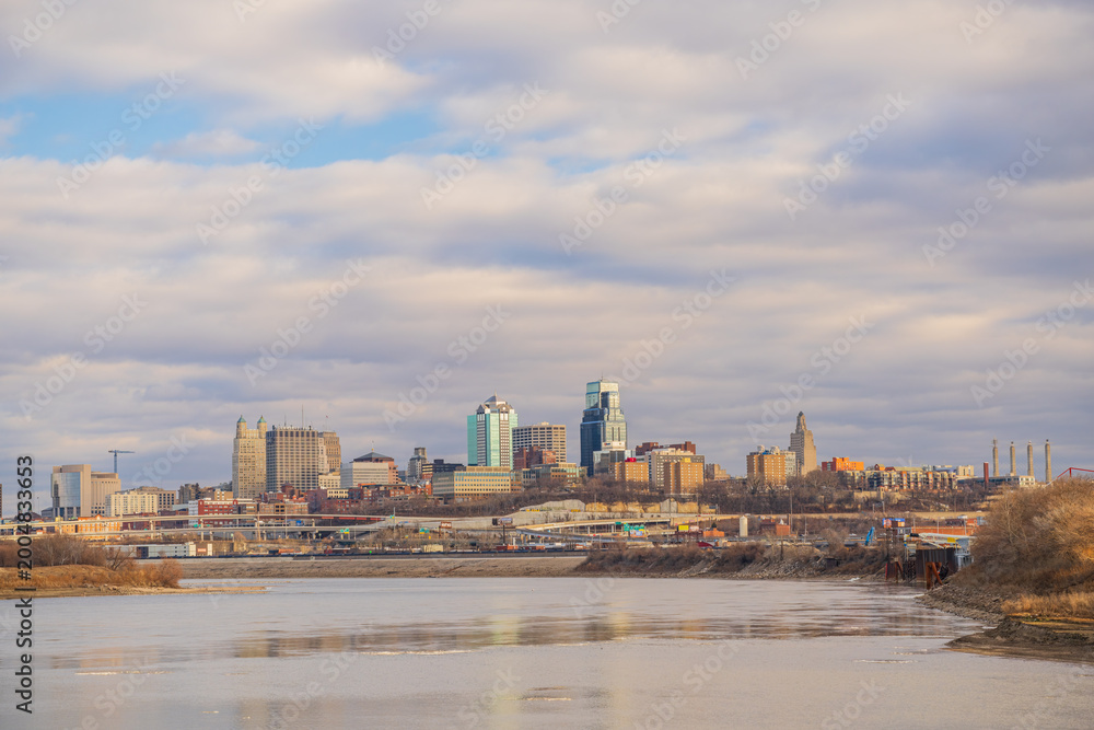Fototapeta premium The skyline of Kansas City rises above the river under a cloudy sky.