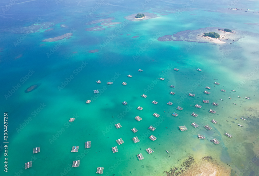 Fototapeta premium Aerial view of dozens of floating net cages (keramba) scattered across the turquoise waters of Tanjung Binga Beach, Belitung, Indonesia, used by traditional fishermen