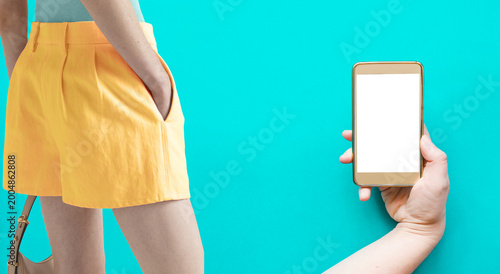 Modern fashion and technology concept featuring a stylish female model in contemporary outfit with striped blouse andyellow skirt, paired with a hand holding smartphone mockup with blank chroma screen