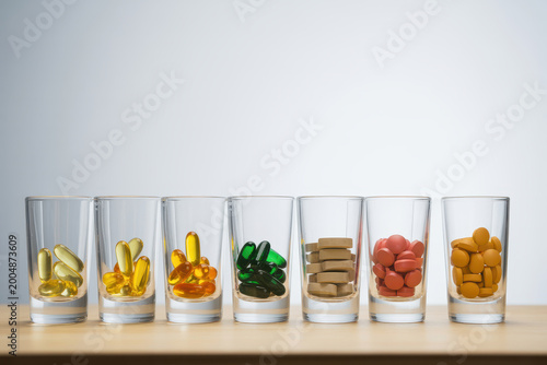 Seven glass shot glasses filled with different types of pills and supplements on wooden table