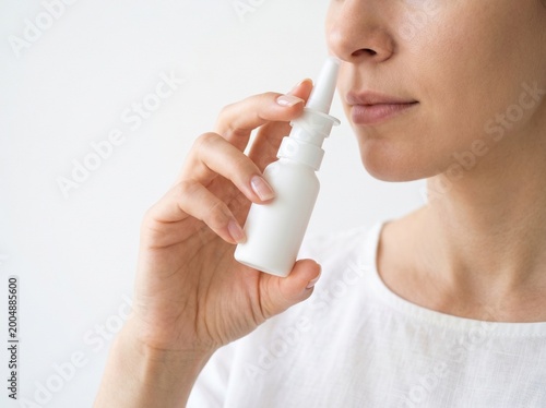 A woman using a nasal spray to relieve congestion. She holds the bottle and aims the nozzle toward her nostril