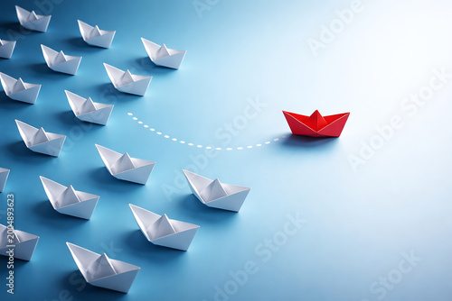 Red paper boat leading a fleet of white boats on a blue background symbolizing leadership business success teamwork innovation uniqueness and moving forward to victory