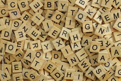 Pile of wooden tiles with various letters in big amount scattered on white board, closeup view