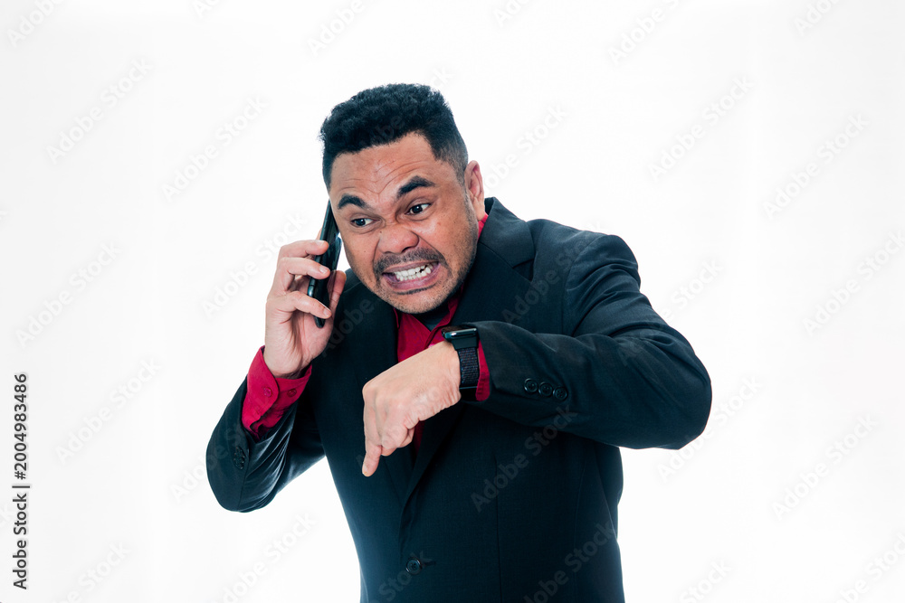 Naklejka premium Portrait of a furious businessman in a black suit shouting on a smartphone while pointing his finger down to the floor, isolated on a white background, representing authority, demanding presence, and 