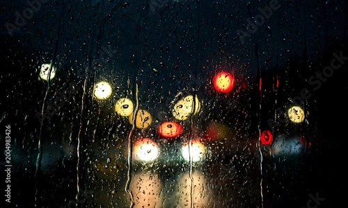 Bokeh effect of blurred car lights at night seen through a rain-streaked window, creating a moody and atmospheric urban scene